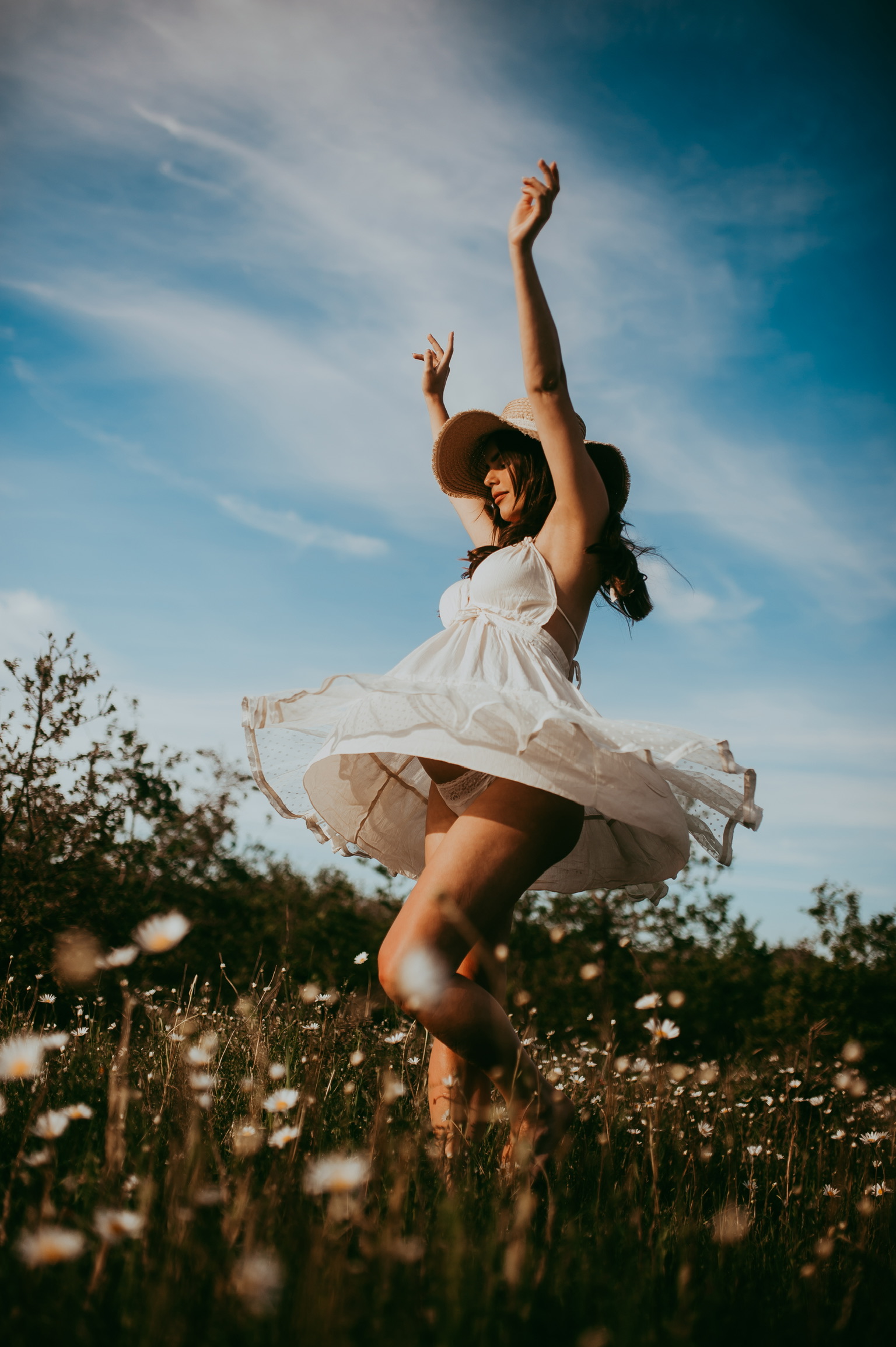 Woman in a white dress raising her arms and dancing freely under a blue sky — empowerment photography session capturing confidence, joy, and feminine freedom.