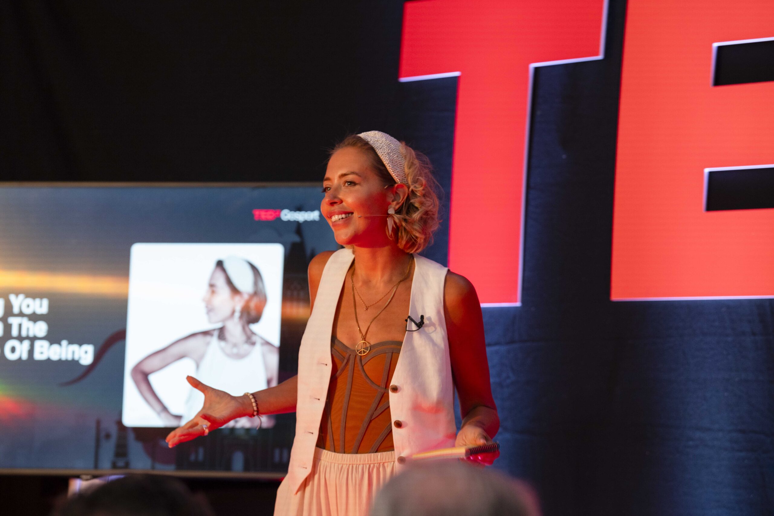 Jen Channer speaking on stage at TEDx Gosport, smiling with one hand open to the audience, cue cards in the other.